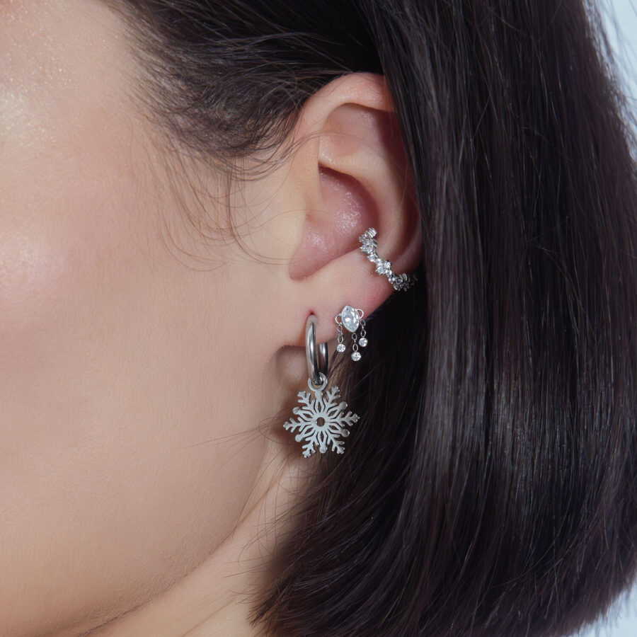 Colgante de cristal plateado en la oreja con otros piercings sobre fondo blanco