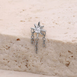 Accesorio de piercing en forma de estrella plateada con cadenas sobre superficie de piedra clara