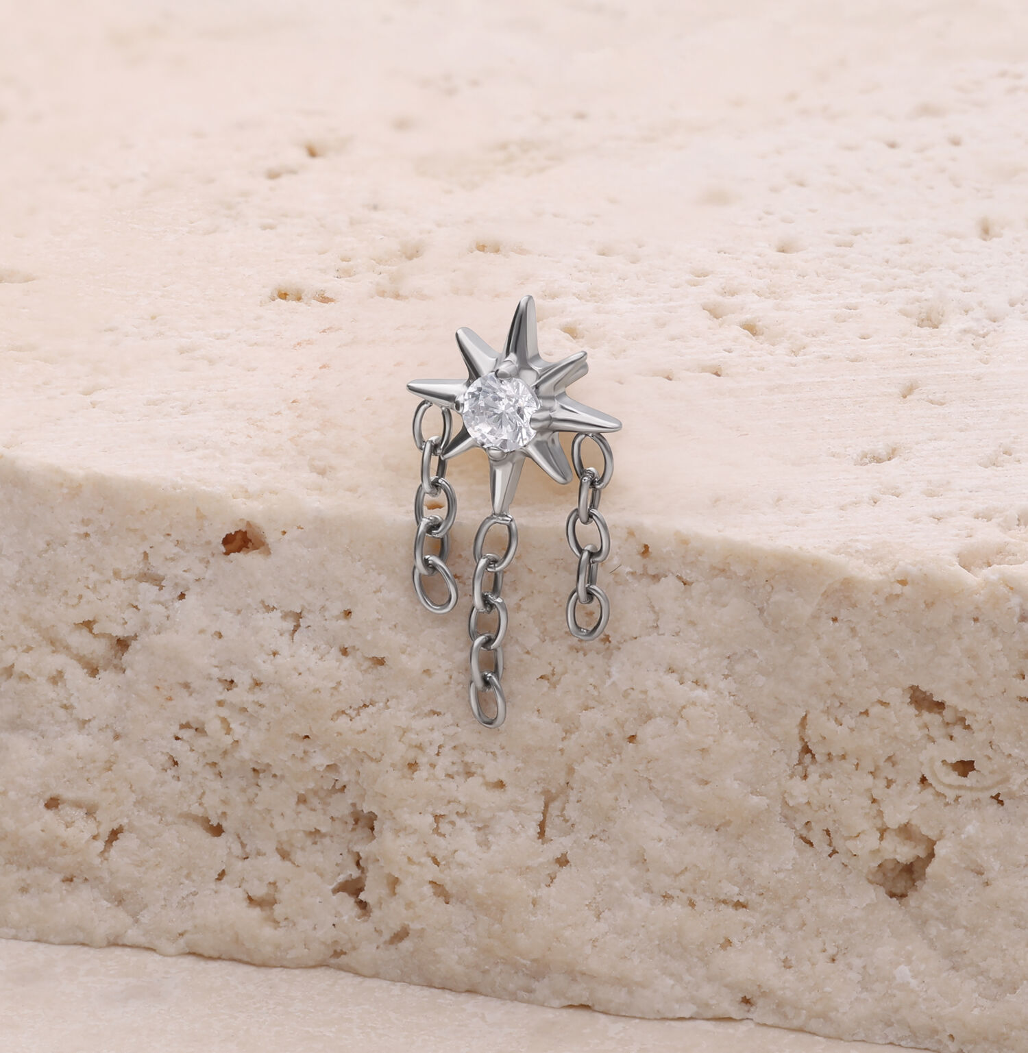 Accesorio de piercing en forma de estrella plateada con cadenas sobre superficie de piedra clara