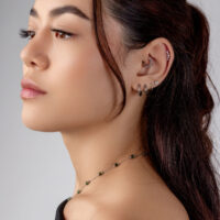 Piercing Helix de Plata con Cristales Mujer con varios piercings de plata en la oreja, incluyendo un Helix adornado con cristales, sobre un fondo gris.