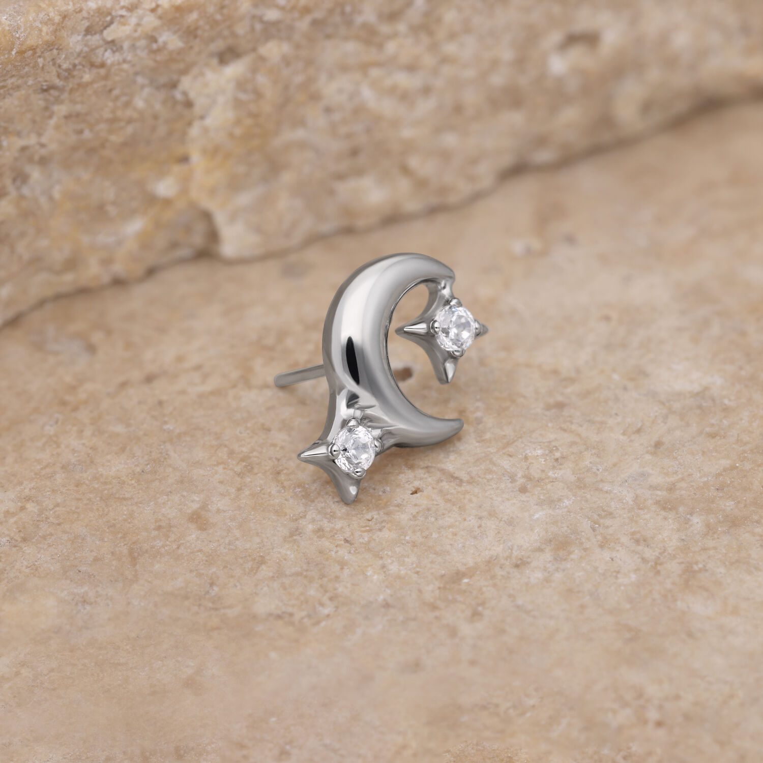 Accesorio de piercing de luna plateada con cristales Accesorio de luna plateada con piedras cristalinas sobre fondo de piedra beige