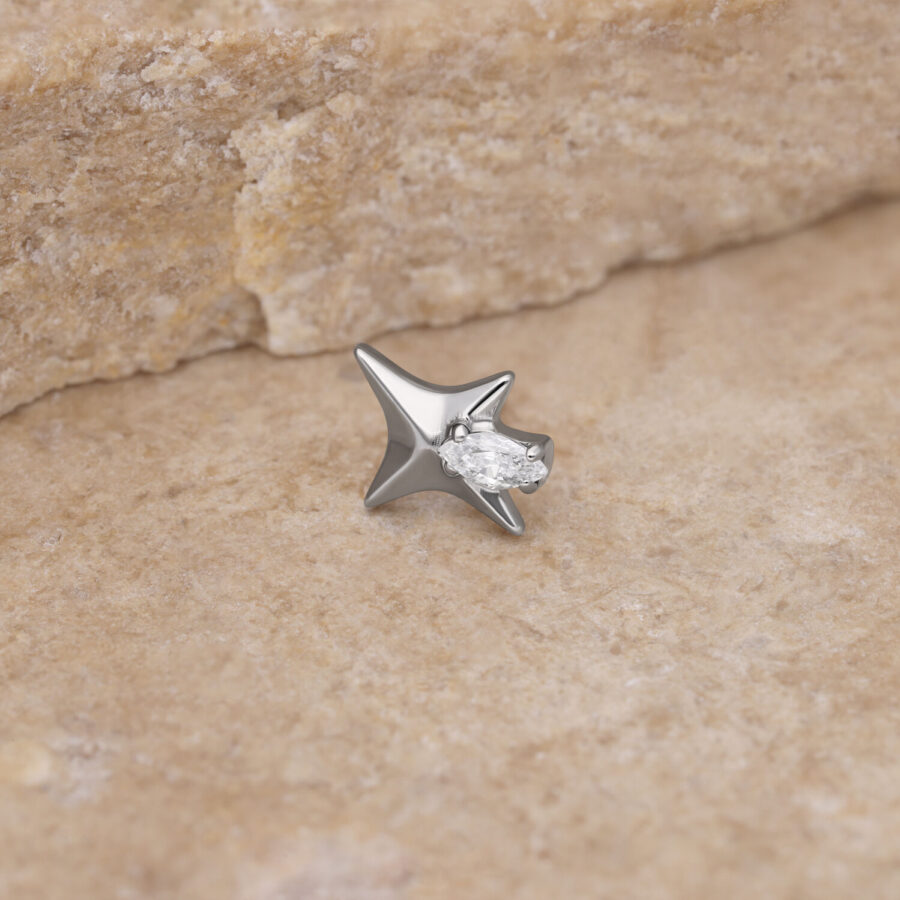 Punta de estrella plateada con cristal claro sobre piedra beige