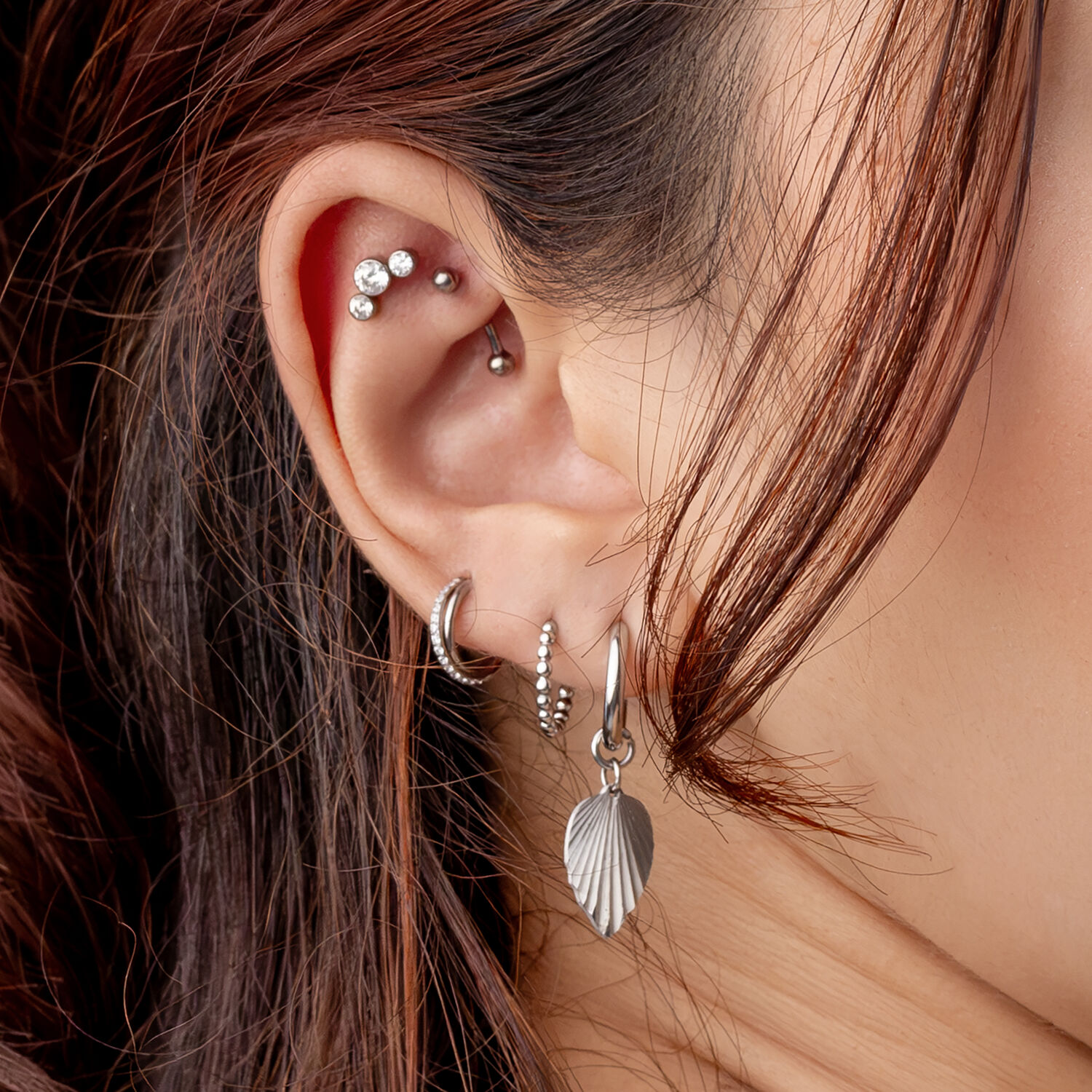 Primer plano de una oreja con varios piercings de plata y tachuelas de cristal, cabello en el fondo