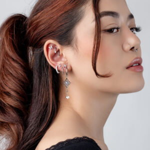 Mujer con varios accesorios de piercing plateados en la oreja, perfil lateral sobre fondo gris