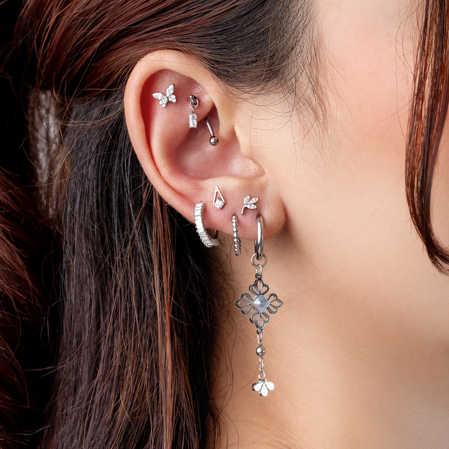 Piercings de oreja plateados con diseño de mariposa Oreja con varios piercings plateados, incluyendo un colgante de mariposa, sobre fondo claro