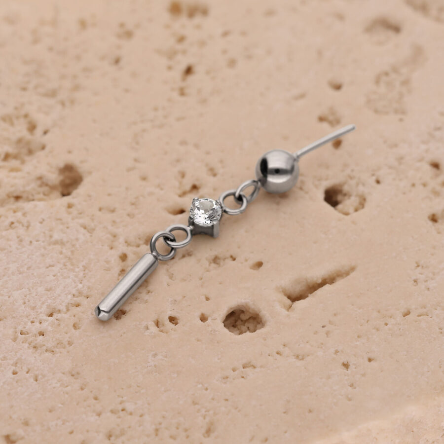 Accesorio de piercing plateado con cristal redondo y pequeño poste sobre estructura beige