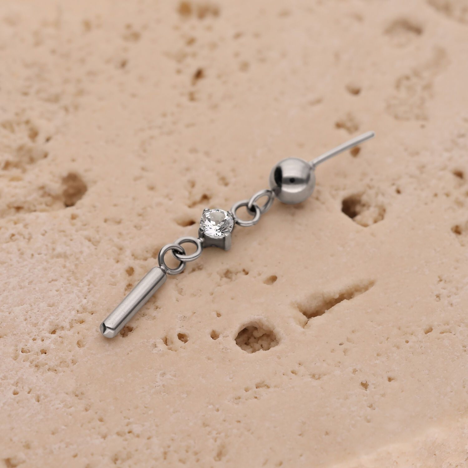 Accesorio de titanio plateado con cristal Accesorio de piercing plateado con cristal redondo y pequeño poste sobre estructura beige