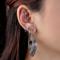 Piercings de plata con cristales Oreja con varios piercings de plata, incluyendo un gran pendiente redondo con diseño floral y cristales claros.