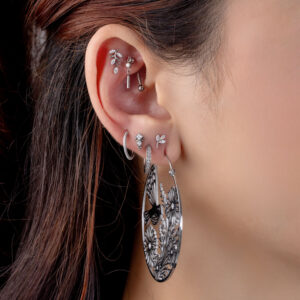 Oreja con varios piercings de plata, incluyendo un gran pendiente redondo con diseño floral y cristales claros.