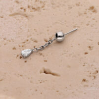 Colgante de piercing de oreja plateado con cadena Colgante plateado con cadena y cristal ovalado sobre fondo beige