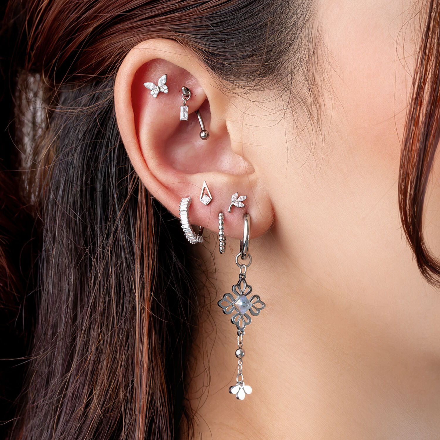 Piercings de plata con cristales Primer plano de una oreja con varios piercings de plata, incluyendo un diseño colgante floral y cristales brillantes.