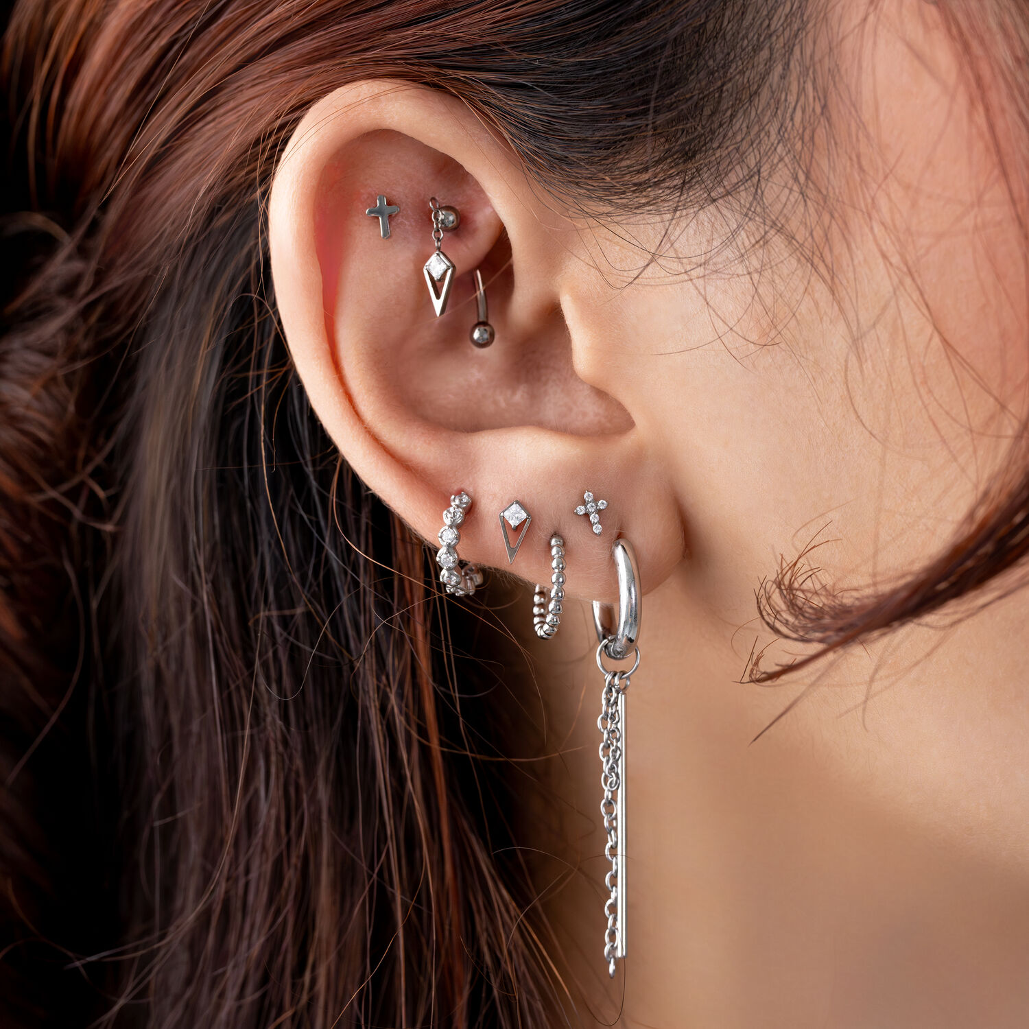 Pendientes de plata con cristales y colgantes Primer plano de una oreja con varios pendientes de plata, cruz, bolas y cadena