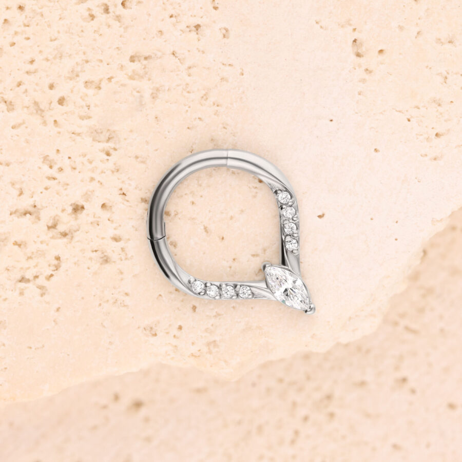 Anillo de piercing plateado con cristales sobre fondo beige texturizado