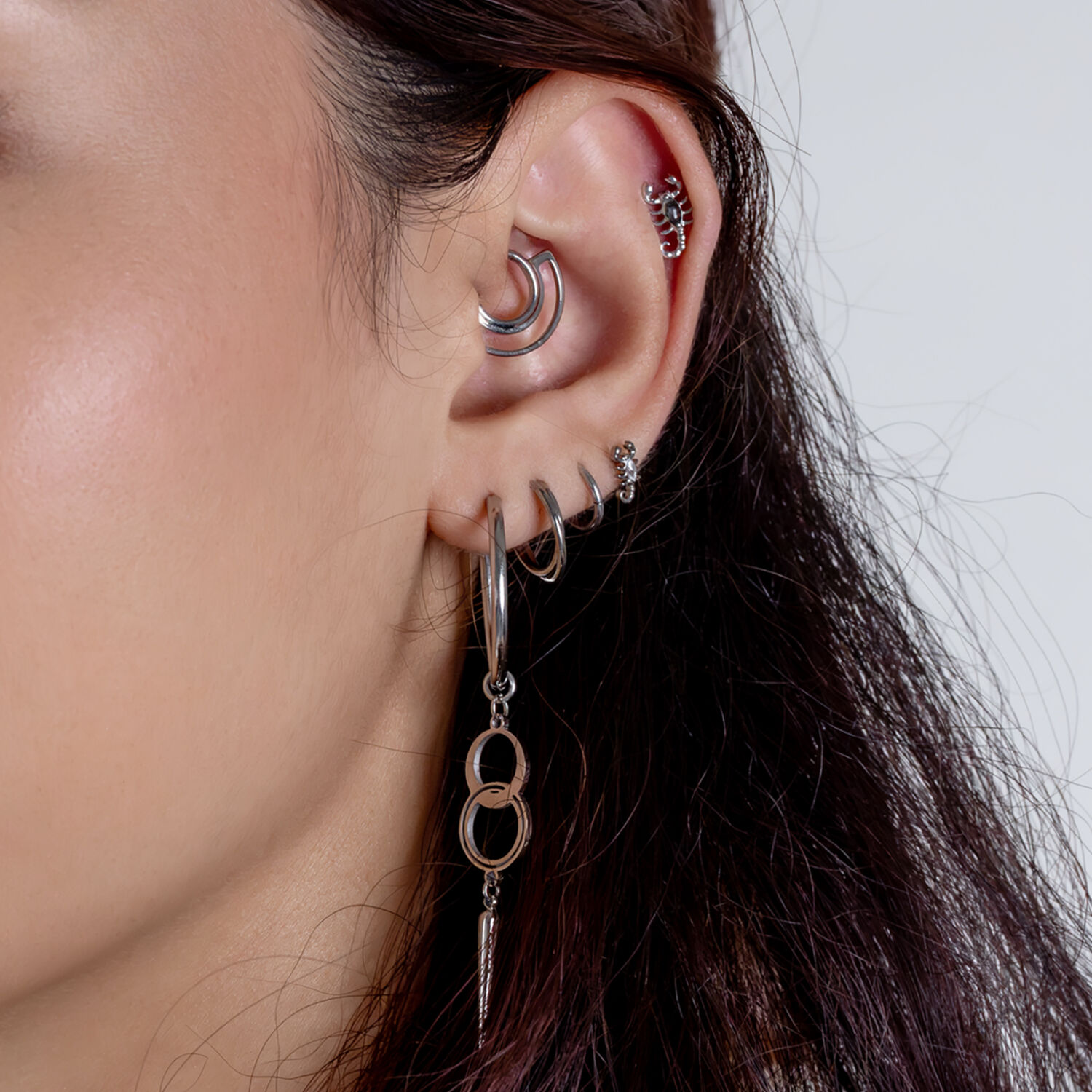 Piercings de plata para orejas con aros Primer plano de una oreja con varios piercings de plata y joyería colgante