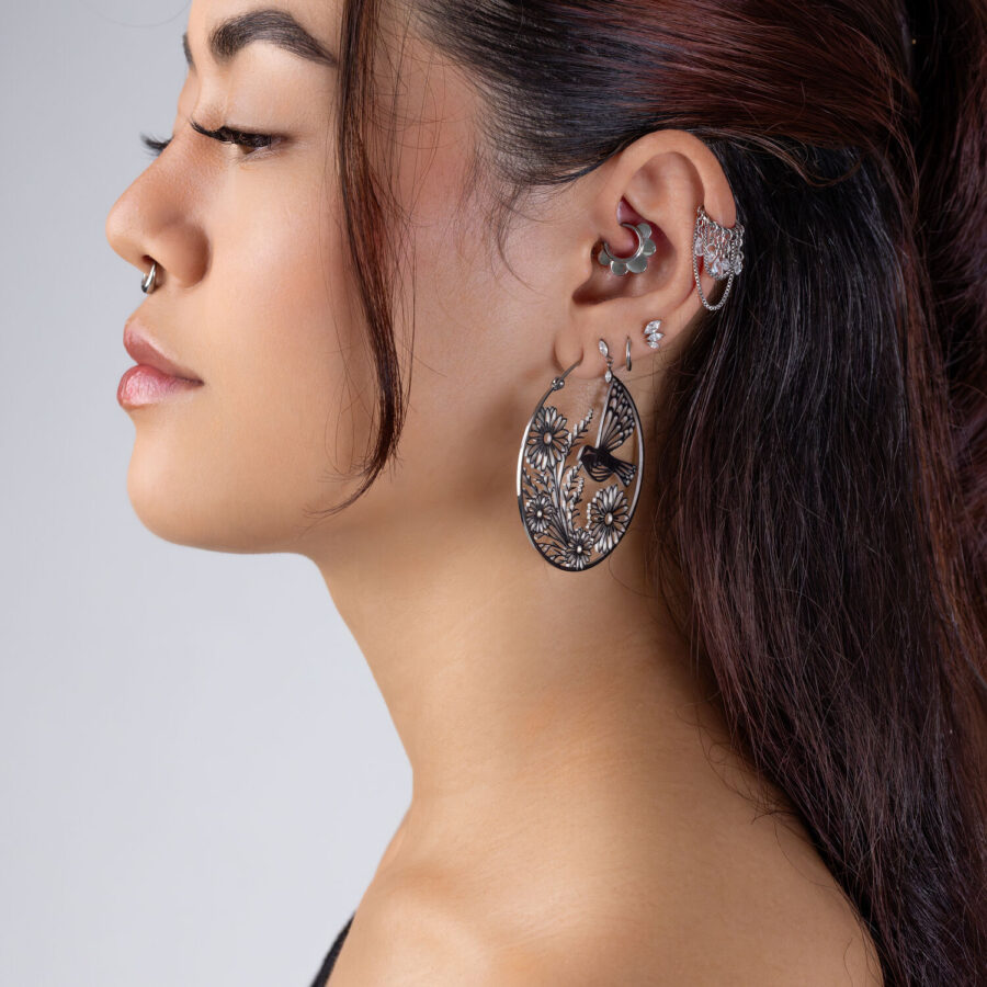 Perfil de una persona con varios pendientes, incluyendo un gran Clicker Half Flower negro con diseño floral.