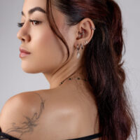 Aro de Marquise Plateado en la Oreja Mujer con varios piercings plateados en la oreja, cabello castaño, tatuaje en el hombro