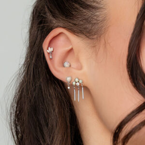 Primer plano de una oreja con varios piercings, incluyendo un aro de ópalo en oro blanco