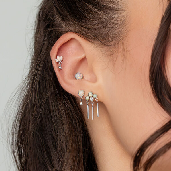 Primer plano de una oreja con varios piercings, incluyendo un aro de ópalo en oro blanco