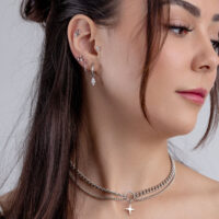 Primer plano de una mujer con varios pendientes de plata y un collar, fondo claro