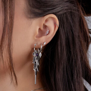 Primer plano de una oreja con varios piercings de plata y un colgante largo, cabello al fondo
