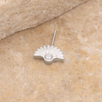 Aro de piercing de oro blanco con piedra cristalina sobre fondo de piedra beige