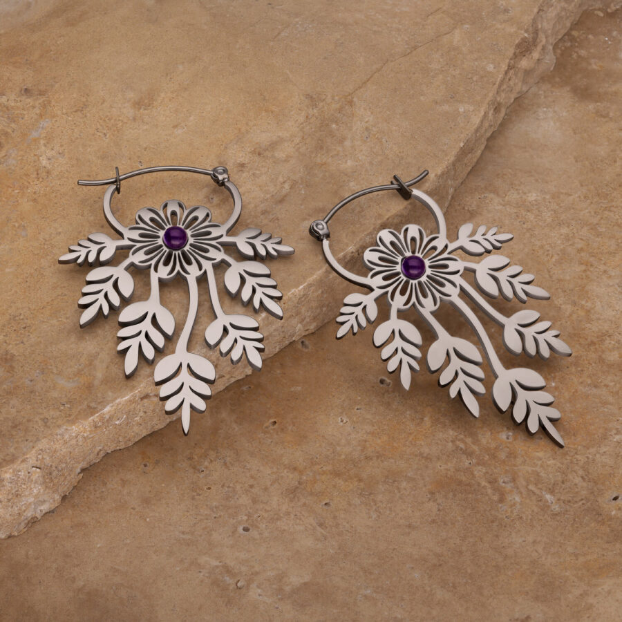 Dos pendientes florales con amatista sobre un fondo rocoso