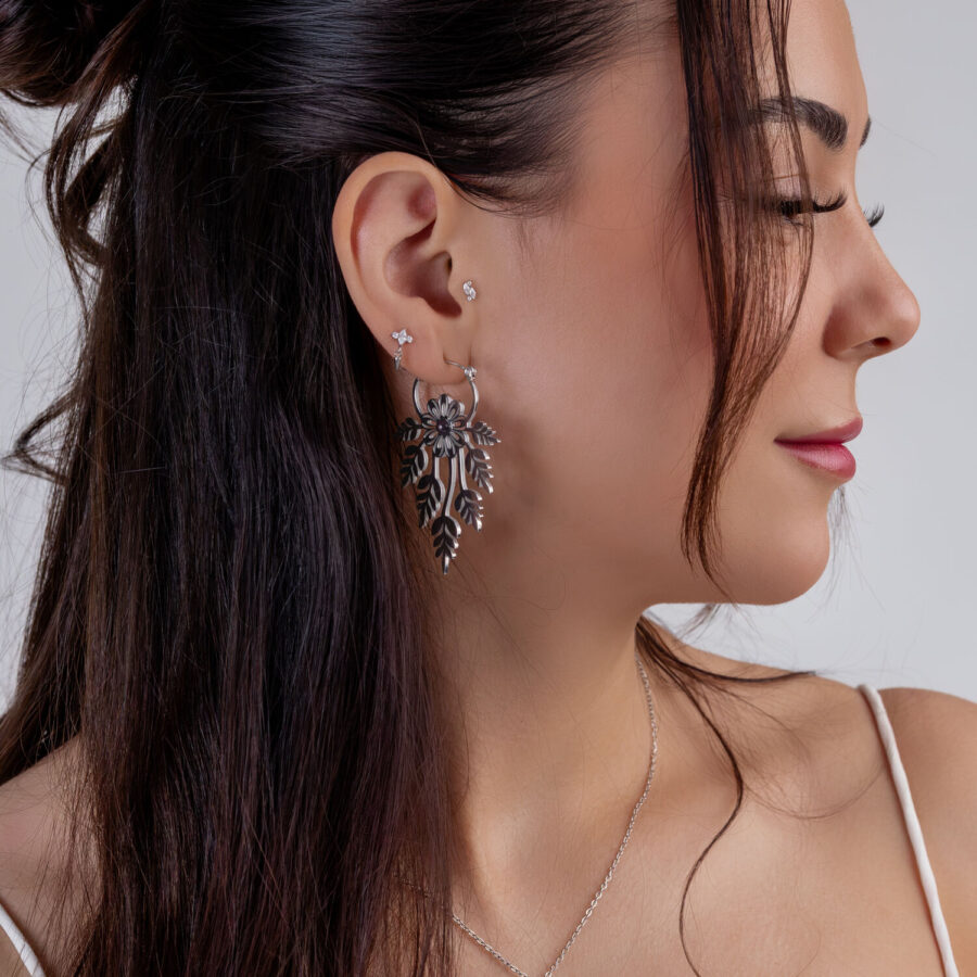 Mujer con cabello largo lleva grandes pendientes de flores plateadas y un pequeño piercing de estrella en la oreja, perfil lateral